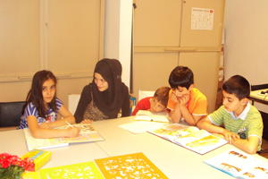 Vier Kinder und eine junge türkische Frau sitzen um einen Tisch und lernen