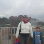 Bild - Mutter und Kind auf eine Plattform bei diesigem Wetter, im Hintergrund ein Urzeittier