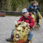 Bild - Kind reitet auf einer Urzeittier-Attrappe auf dem Spielplatz