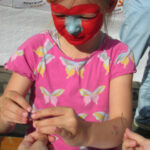 Bild - Kind mit bemaltem Gesicht bastelt eine Halskette