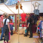 Bild: Auf dem Kleiderbasar probieren zwei Mädchen Kleidung an, unterstützt von der Mutter und dem Händler.