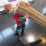 Bild: Junge versucht mit einem übermannsgroßen Buntstift auf dem Fußboden zu schreiben