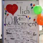 Bild: Flipchart mit Schriftzug "Herzlich Willkommen" und vielen Unterschriften der Anwesenden