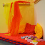 Bild: in einer Ecke des Raumes liegen rote Matratzen mit bunten Kissen und darüber herabhängenden Tücher