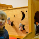 Bild: auf der Kletterburg. Zwei Füße ranken durch zwei Aussparungen in Sternform aus der Kletterburg heraus. Im Vordergrund  schaut ein Junge in Richtung Kamera