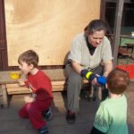 Besuch auf der Weddinger Kinderfarm | © FZM Bild: Mutter mit ihren 2 Kindern spielend an eine Bank