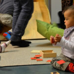 Bild: kleines Kind spielt auf dem Fußboden mit Holztäfelchen