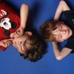 Bild: 2 Jungs liegen Kopf an Kopf auf blauem Hintergrund