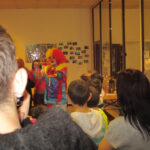 Viel Freude mit dem Clown. | © FZM Bild: ein Clown agiert im Hintergrund. Kinder von hinten im Vordergrund