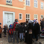 Ausflug zur Domäne Dahlem | © FZM Bild: Die Besuchergruppe des FZ versammelt sich vor dem orang-farbenen Herrenhaus und die Leiterin hält eine Rede