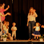 Bild: Kinder und Eltern winkend auf einer Bühne