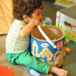 Bild: Kind sitzt vor einem großen Bauklotzeimer und beißt in den Henkel