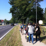 Bild: Gruppe läuft auf einem Weg neben Strasse zum Freizeitpark. Ansicht von hinten.