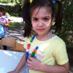 Bild: Mädchen zeigt stolz ihre selbst gebastelte Kette und blickt Betrachter an