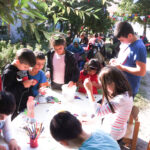 Bild: 8 Kinder basteln und malen an einem Tisch im Freien