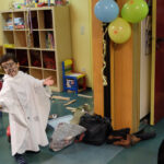 Foto: Kind mit weißem Umhang aus Bettlaken und bemalten Gesicht spukt als Gespenst durch den Raum