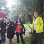 Foto: 5 Frauen im Regen unterm Baum mit Blick zum Betrachter. Ein Frau unter dem Regenschirm