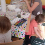 Ferienangebot - Basteln und Malen mit Gips | © FZM Foto: Eltern unterhalten sihc na einem Tisch, Kinder malen dabei