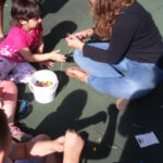 Foto: Kinder und Erzieherin sitzen auf der Erde und fertigen Perlenketten