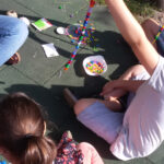 Foto: Kinder und Erzieherin sitzen auf der Erde und fertigen Perlenketten