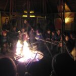 Foto: Kinder und Eltern sitzen im Dunklen um ein Feuerschale und backen Stockbrot.