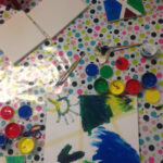 Foto: Tuschezeichnungen und Tuschefarbtöpchen auf einem Tisch mit bunt bepunkteter Tischdecke