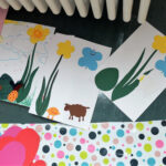 Foto: bunt bemalte Bilder liegen zum Trocknen auf dem Fußboden, vor einem Heizkörper.