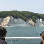 Foto: Blick auf den Kreisefelsen in Rügen von einem Schiff aus. SAm unteren Rand Schiffsgeländer und 3 Köpfe von hinten.