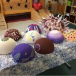 Foto: 9 bunt bemalte Styropor-Halbkugeln auf einem Tisch mit blau gemusterter Tischdecke