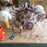 Foto: auf eine Tisch zwei weiße Styropor-Halbkugel im Hintergrund, eine bemalte und beklebte Styropor-Halbkugel mittig. Davor und dazwischen Malzeug.