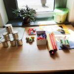 Foto: 6 Blechdosen in Pyramide aufgebaut, daneben Bastelzeug auf einem Tisch vor einem Fenster.