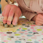 Foto: Kinderhände beim austechen von Plätzen aus Teig mit Sternfigur auf einer bunt bepunkteten Tischdecke