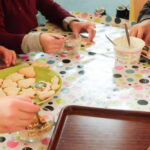 Foto: Kinderhände beim verzieren von Plätzen mit Zuckerguß und bunten Streuseln auf einer bunt bepunkteten Tischdecke
