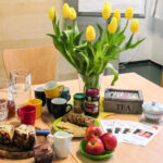 Eindrücke vom Familiencafé im Familienzentrum Foto: Tisch mit Kuchen, Äpfeln, Tassen und Gläsern, Teeschachtel und Blumenstauß in Vase