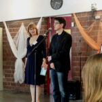 Fünf Jahre Familienzentrum Moabit-Ost - Die Leiterin Sibylle Büchele mit der Stadträtin Frau Dr. Obermeyer | Foto: © FZM Foto: Die Leiterin Sibylle Büchele im Hinmtergrund mit der Stadträtin Frau Dr. Obermeyer auf der Bühne vor einem Mikrofon.