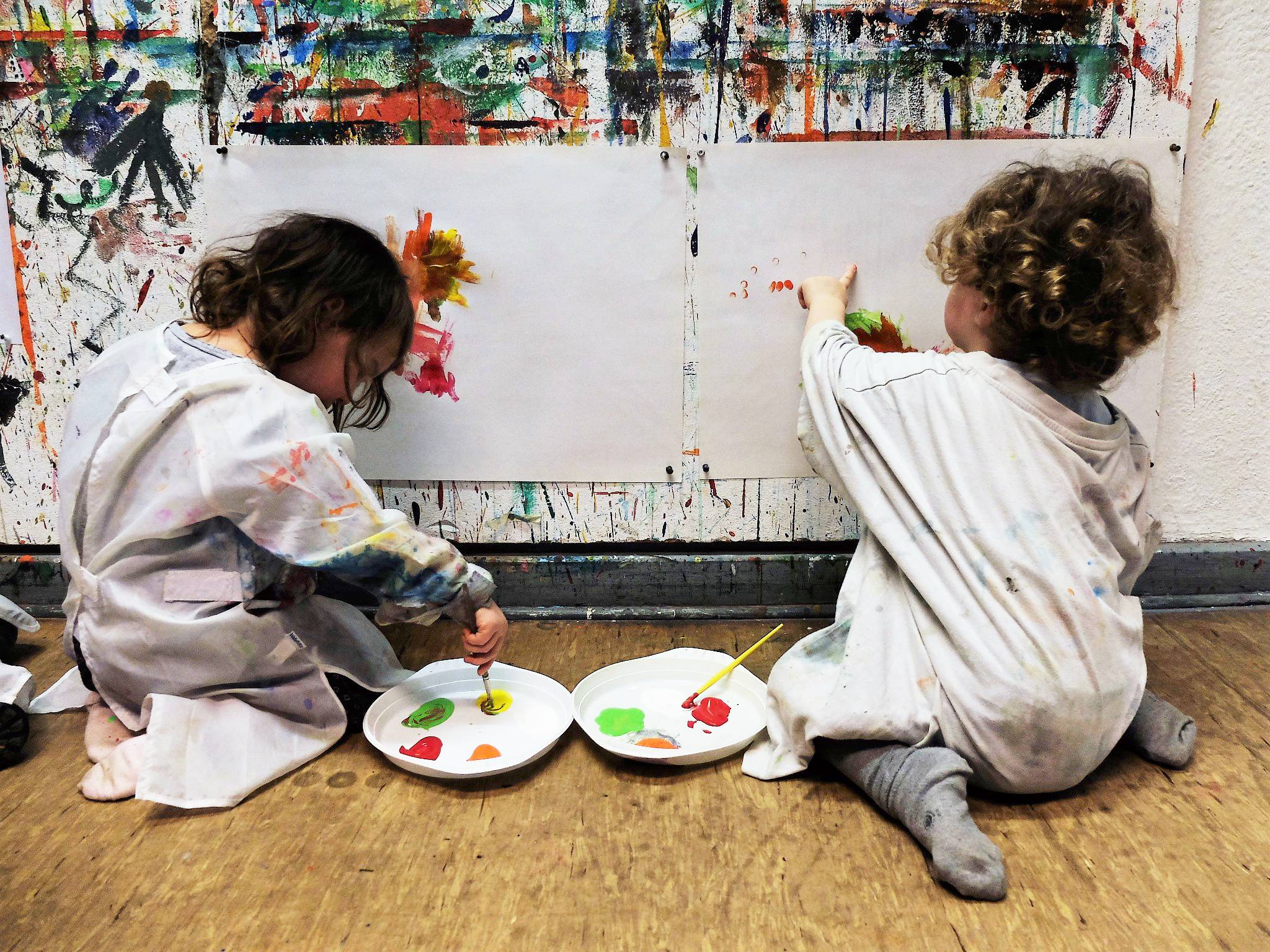Foto: zwei Kinder malen an einer Wand, auf der ein Blatt Papier aufgespannt ist