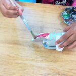 Foto: Hand rechts hält Klopapierrolle und eine Hand links malt diese mit einem Pinsel rot an