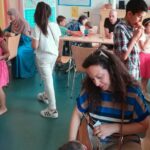 Viele Menschen besuchen das Sommerfest Foto: Raum mit Tisch und Stühlen um und an dem Erwachsene und Kinder sitzen und stehen