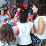 Foto: Rechts im Bild ein Tisch an eine Erwachsene Frau mit Kindern sitzt, im Hintergrund sitzen Menschen