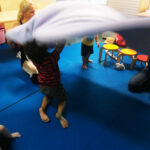 Foto: vier Personen, zwei davon Kinder, schwingen eine Decke nach oben