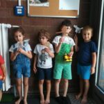 Foto: fünf Kinder stehen vor einer dunklen Backsteinwand und halten Stäbe mit gebastelten Figuren