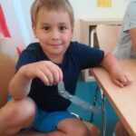 Foto: Ein Junge sitzt auf einem Stuhl und hält eine silberne, gebastelte Schlage in der rechten Hand