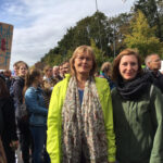 Foto: Menschenansammlung davor zwei Frauen, links mit gelber, rechts mit grüner Jacke