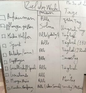 Bild: Tafel mit einem Aufgabenplan in schwarzer Schreibschrift, Überschrift ist Ziel der Woche