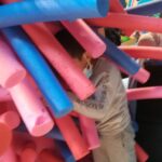 Foto: links ein Berg Schwimmschläuche in das ein Kind von rechts reinspringt