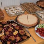 Foto: Tisch aus der Vorgelperspeltive, auf ihm mehrere Speisen, in der Mitte ein Kuchen