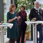 Foto: drei Menschen vor einem Stehtisch, alle lachen