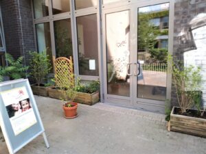 Foto: Eingang des Familienzentrums von außen mit Blumenkübeln und Aufsteller